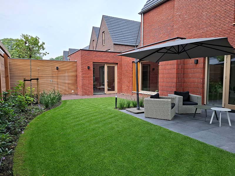 professionele-tuinaanleg-landgoed-coudewater Natuurlijk aangelegde plantenborder met gevarieerde beplanting naast een houten wand van een tuinberging op Landgoed Coudewater.
